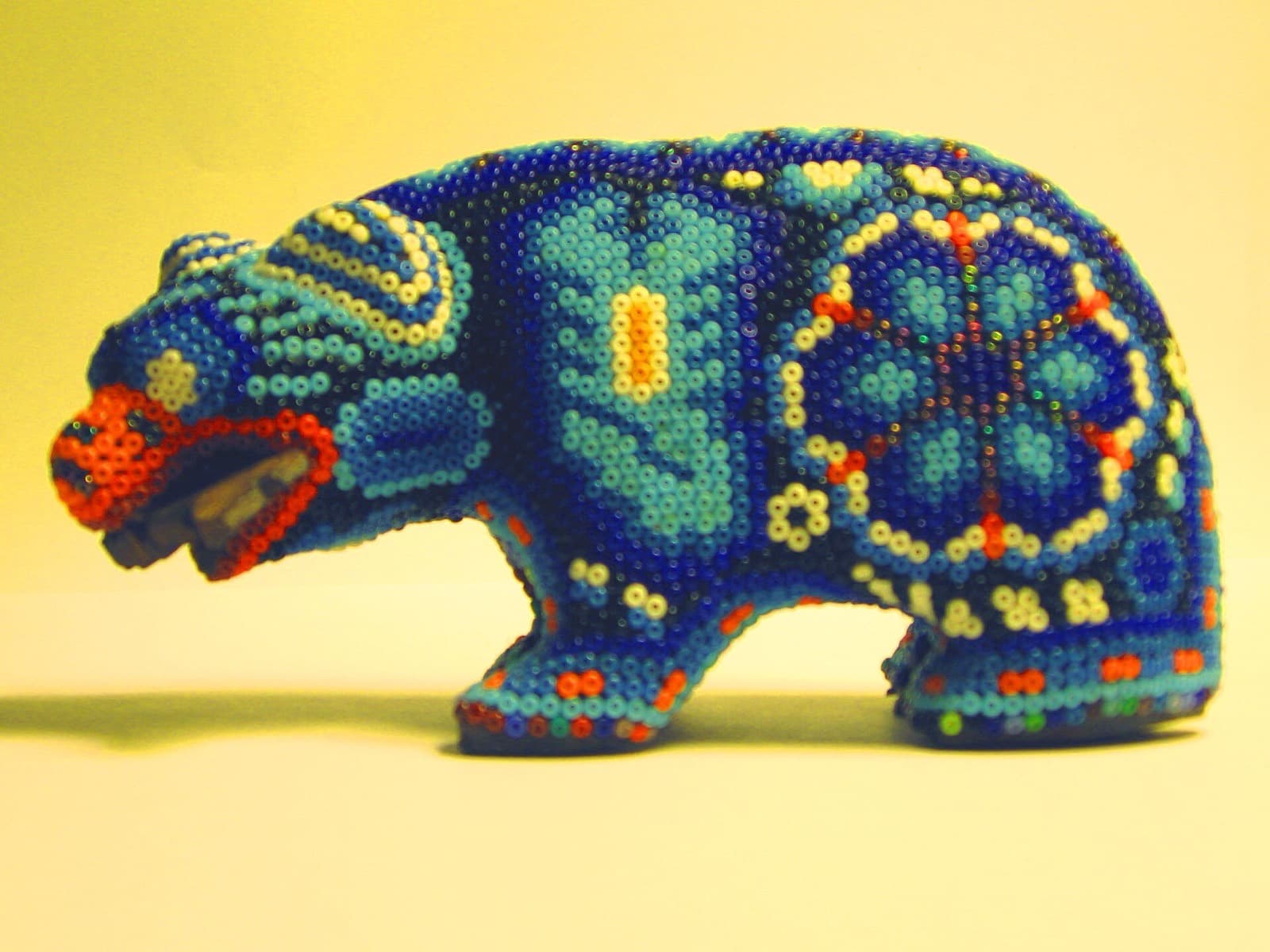 Figura de oso recubierta de chaquira azul con motivos geométricos del arte huichol