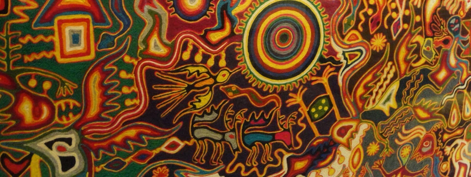 Cuadro de estambre huichol de formato panorámico con un venado, un sol concéntrico y escenas mitológicas en rojo, verde y amarillo