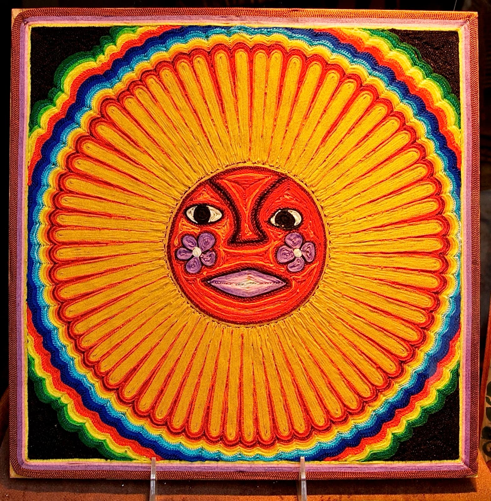 Pieza circular de estambre huichol con un sol radiante de colores concéntricos